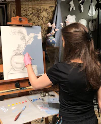 Beginner artist painting a still life of a brown jug and red apples. 